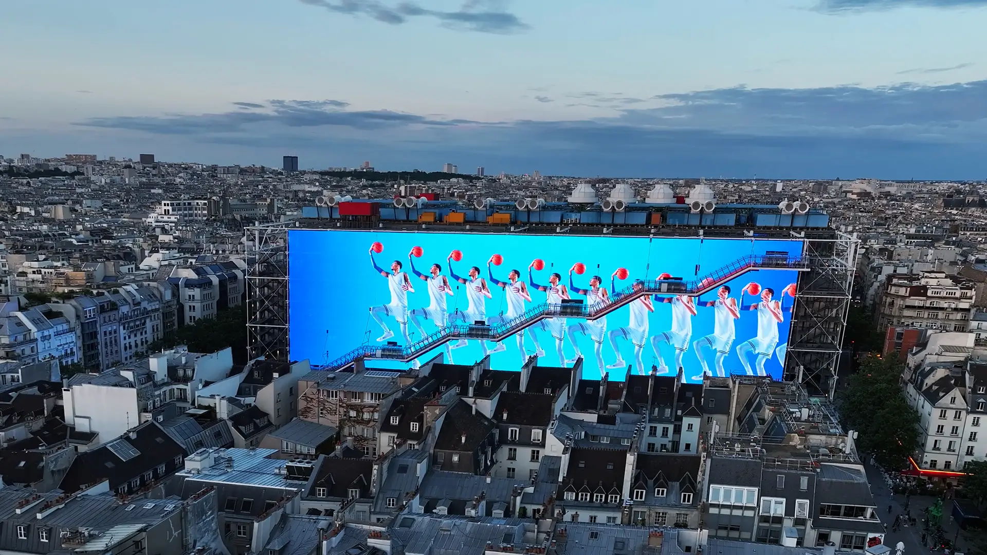 Variation of the giant screen in front of the Centre Pompidou, with basketball players on a electric blue background, wearing NIKE products