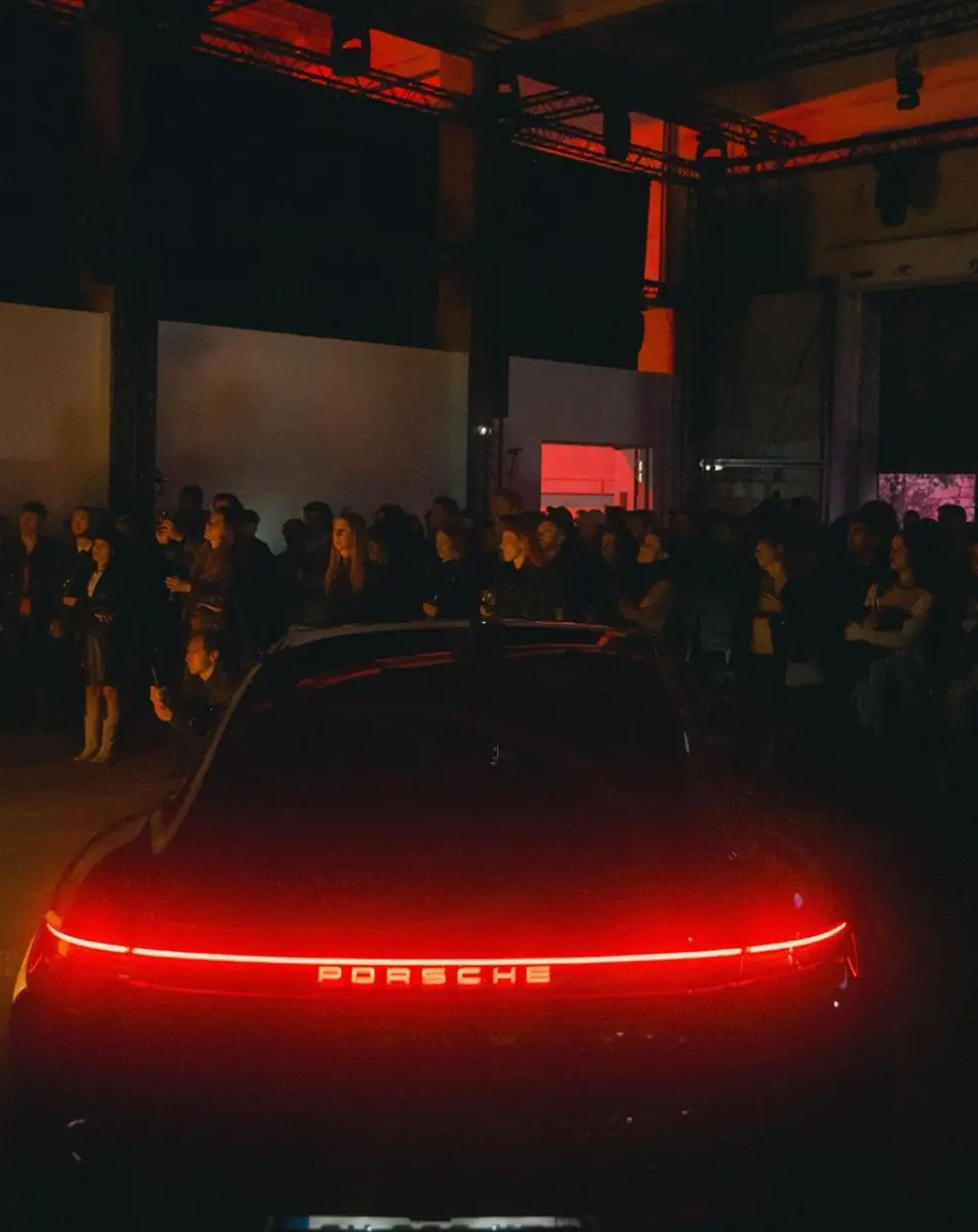 Attendees waiting outside at night to join the festival, Porsche car on display