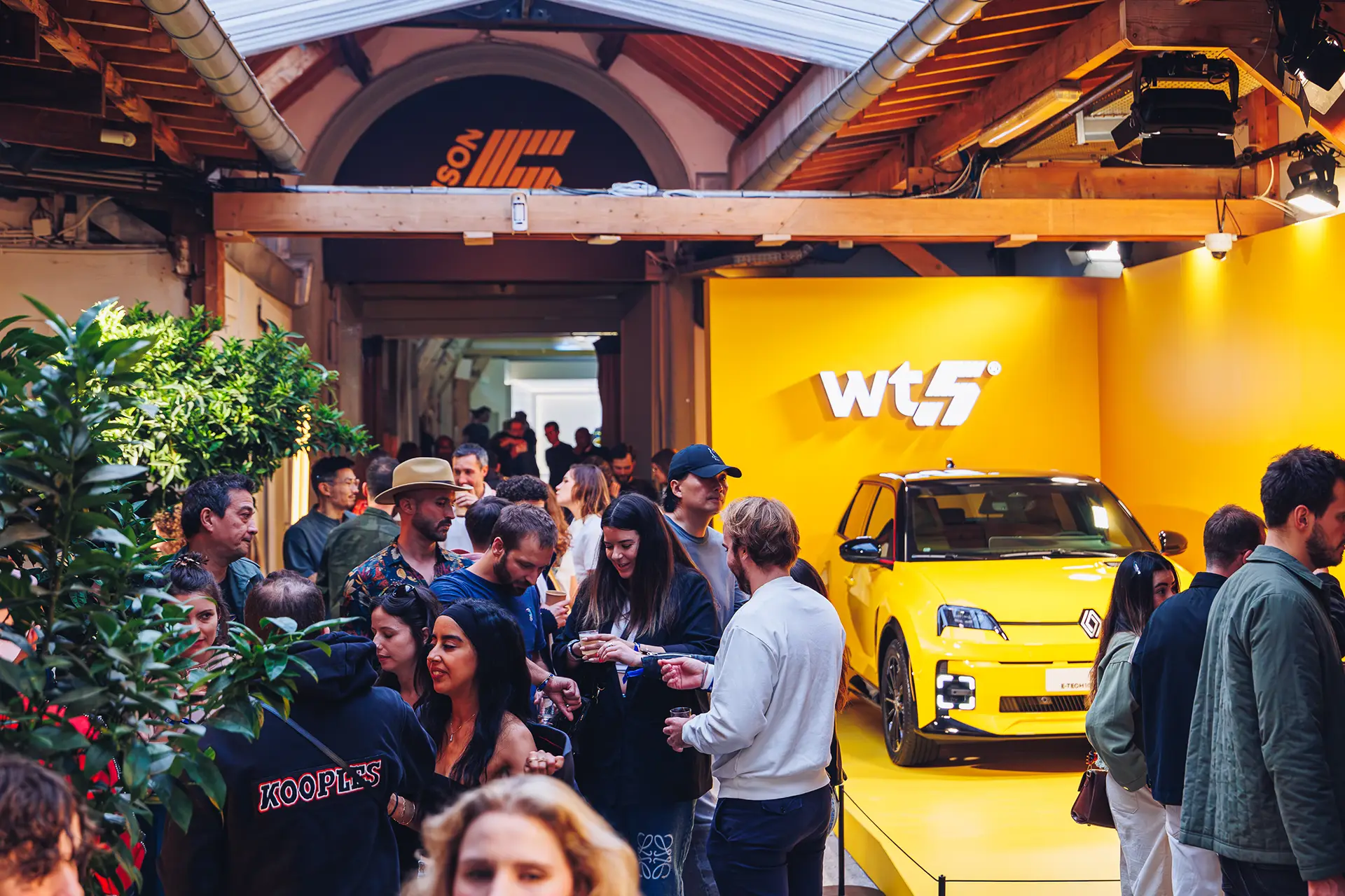 MAISON5 entrance, filled with attendees looking at the yellow Renault 5 E-Tech 100% Electric